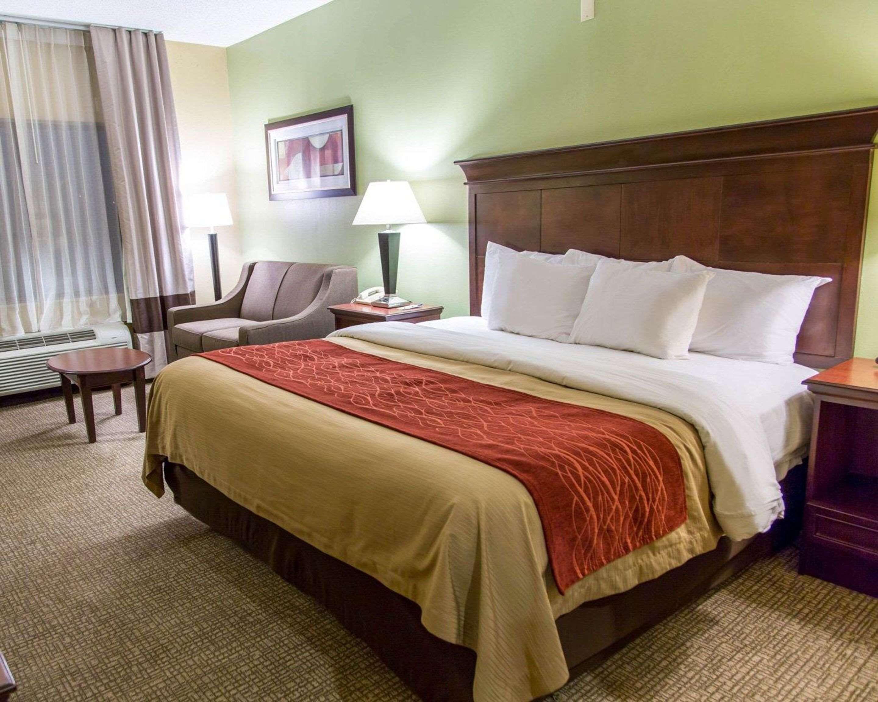 A hotel room with a large bed, a chair, a desk, a lamp, and a window with curtains.