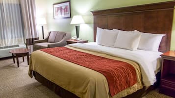 A hotel room with a large bed, a chair, a desk, a lamp, and a window with curtains.