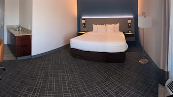 Una habitación de hotel con cama, un escritorio con lámpara, un baño pequeño y una ventana.
