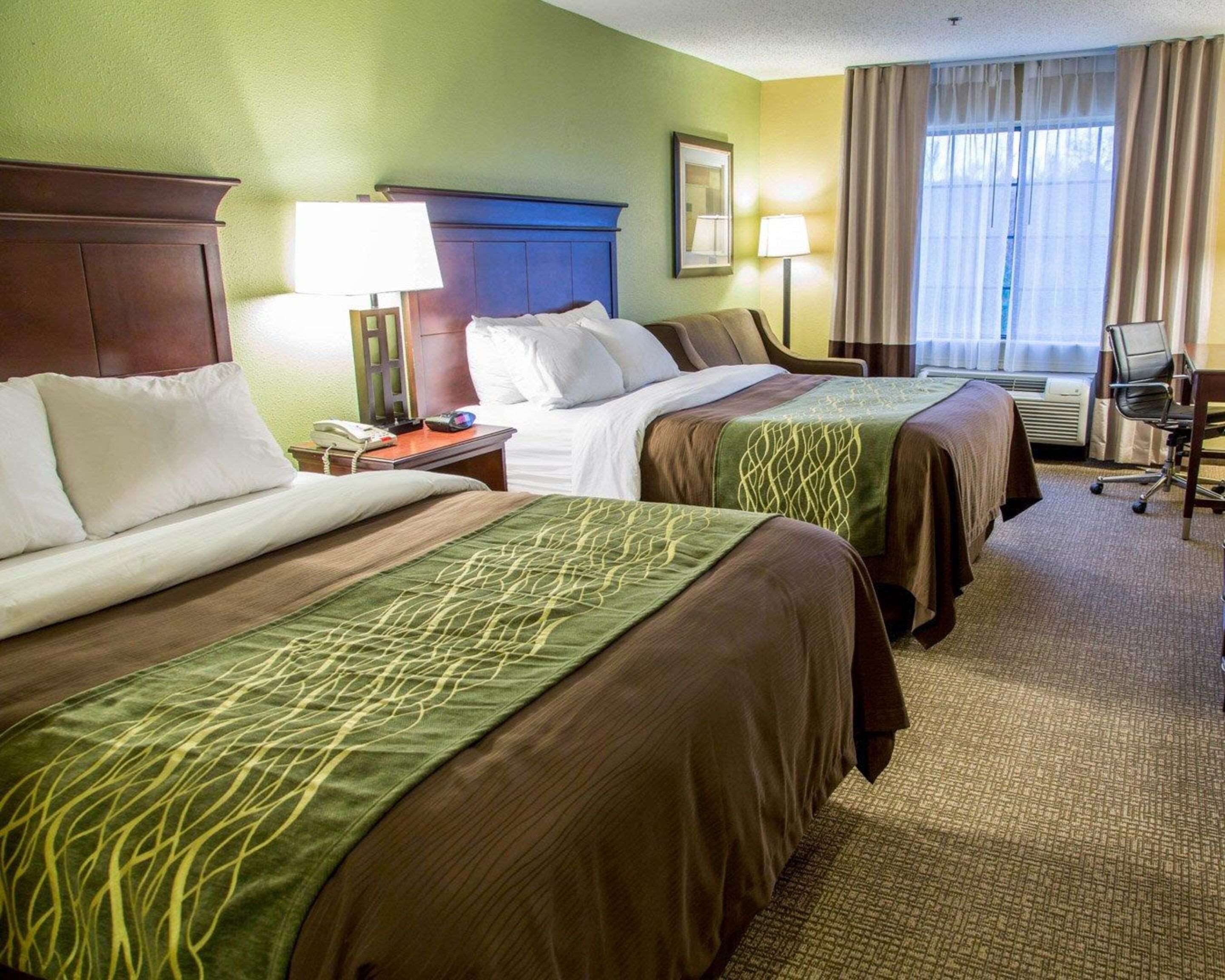 A hotel room with two beds, a desk, a chair, and a window with curtains.