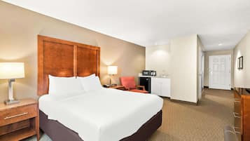 Een hotelkamer met een groot bed, een bureau met lamp, een kitchenette en een deur naar een andere kamer.