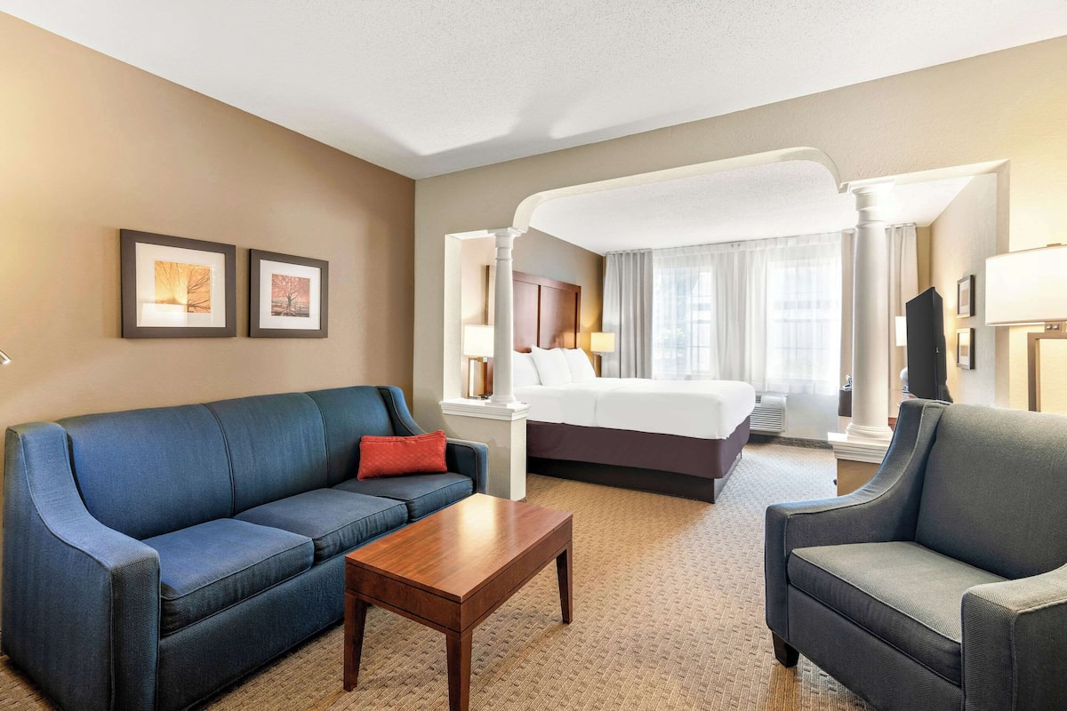A hotel room with a large bed, a blue sofa, a wooden coffee table, and two framed pictures on the wall.