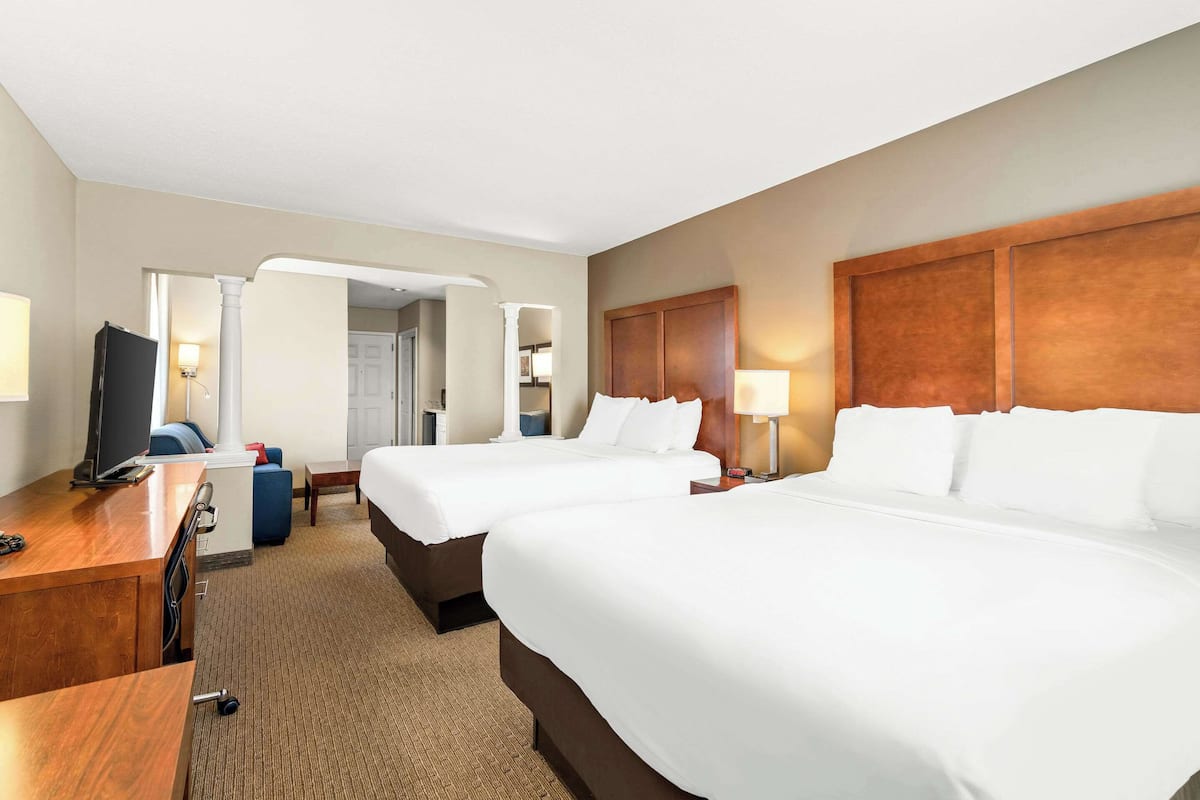 A hotel room with two beds, a desk, a TV, and a bathroom visible through an open door.