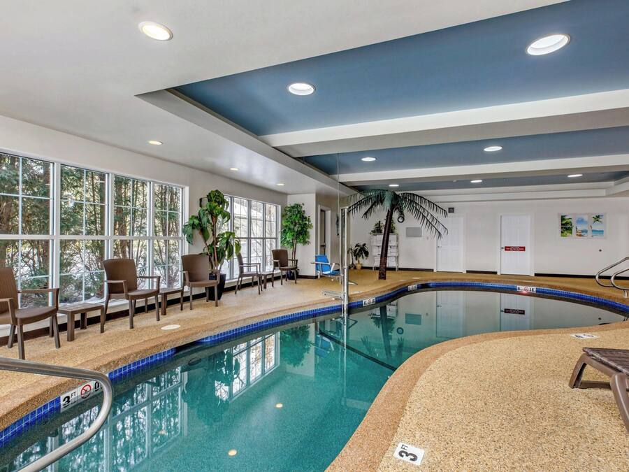 An indoor swimming pool with clear blue water, surrounded by lounge chairs and potted plants.