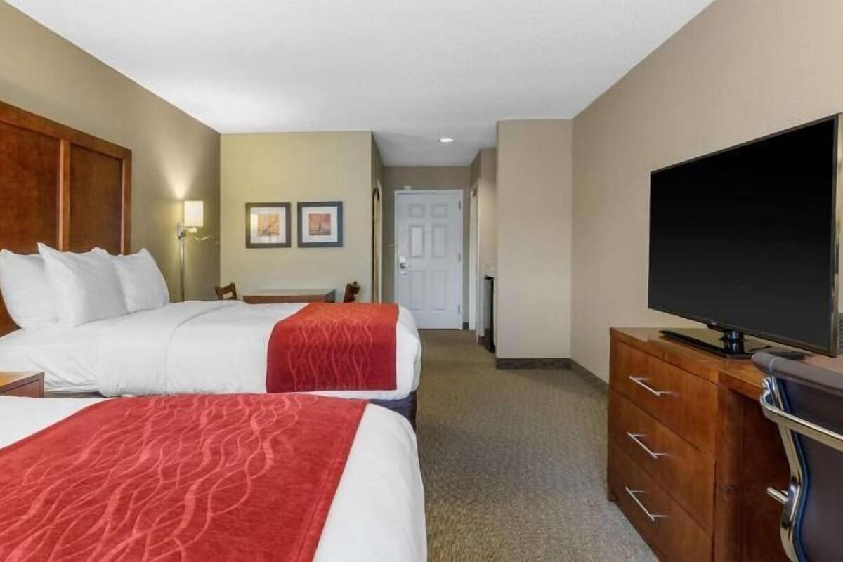 A hotel room with two beds, a television, a dresser, and a hallway leading to a door.