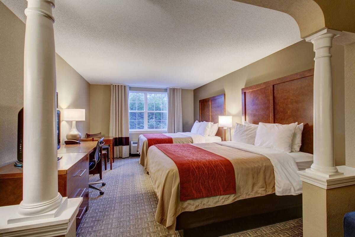 A hotel room with two beds, a desk, a chair, a TV, and a window.