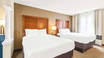 A hotel room with two beds, a large wooden headboard, a nightstand with a lamp, and a large window with curtains.