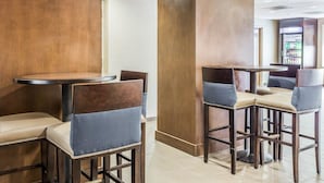 A modern hotel lobby with wooden paneling, round tables, and cushioned chairs. - Comfort Suites at Isle Of Palms Connector (Mount Pleasant)