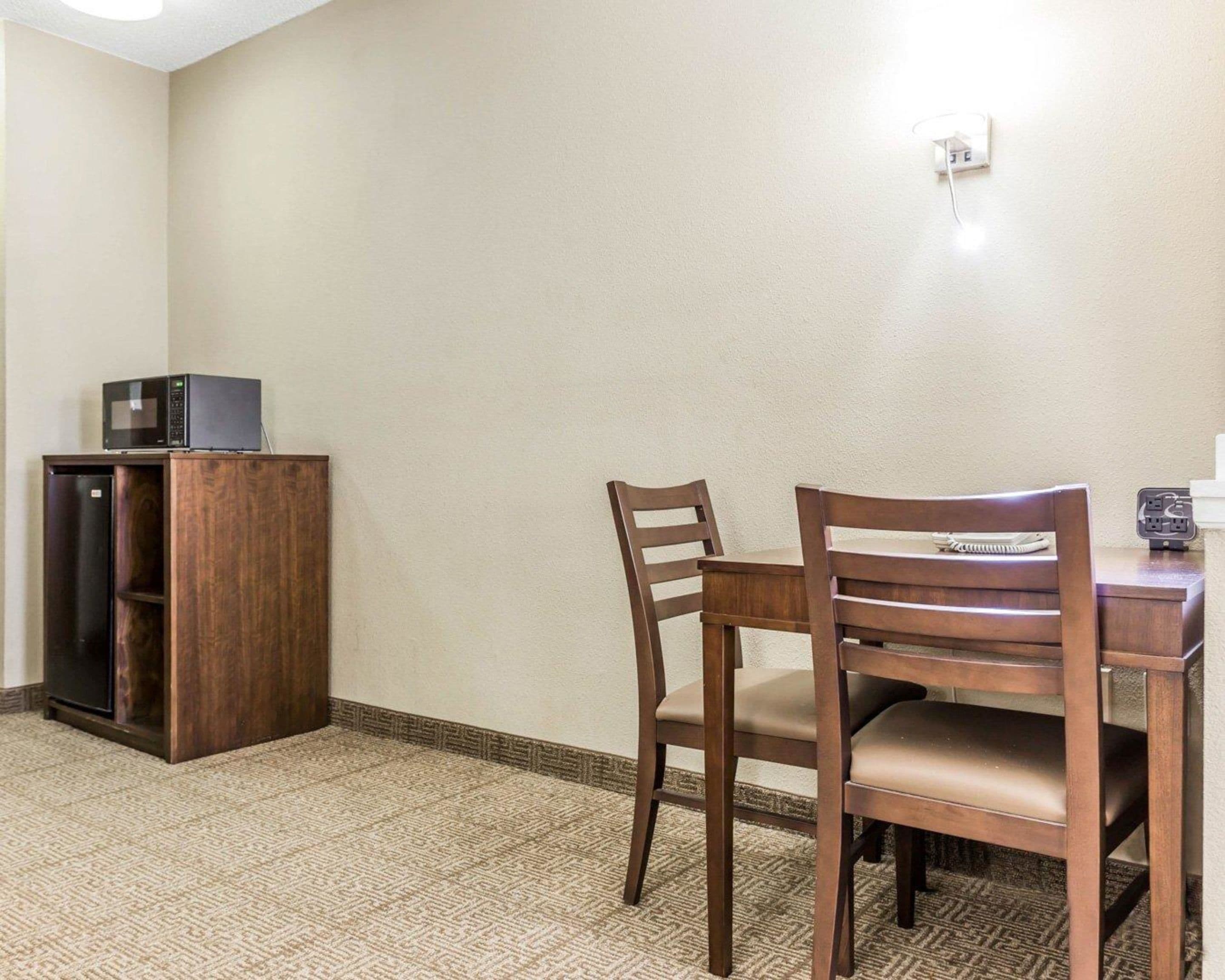 A room with a wooden dining table and chairs, a small wooden cabinet, and a microwave on top.