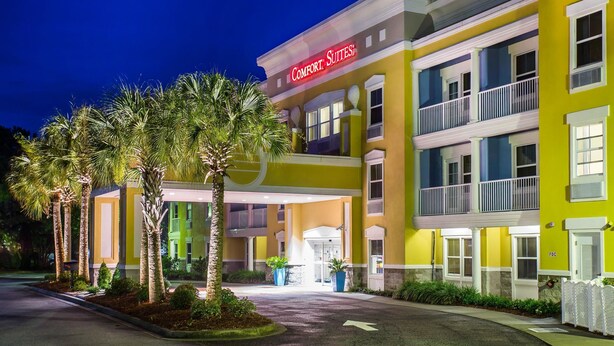 A multi-story hotel with a yellow facade, balconies, and palm trees in the foreground. - Comfort Suites at Isle Of Palms Connector (Mount Pleasant)