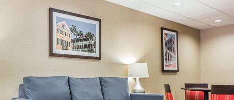 A hotel room with a blue sofa, a patterned rug, a lamp, and two framed pictures on the wall.