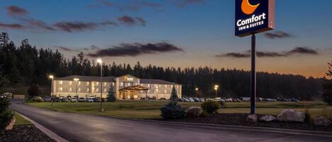 A Comfort Inn & Suites hotel with a well-lit entrance, a parking lot, and a clear view of the surrounding trees and sky.