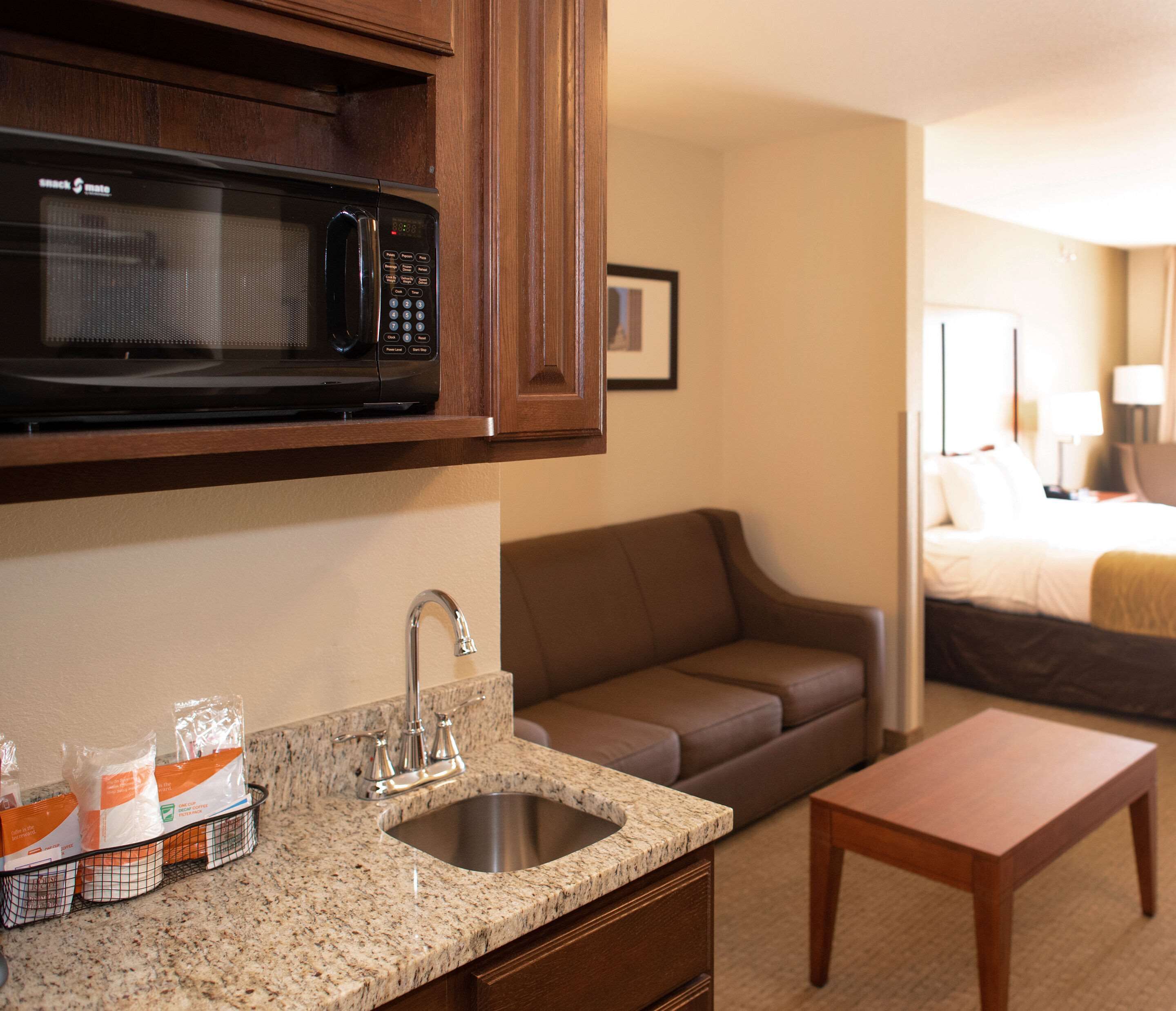 A compact hotel room with a kitchenette, including a microwave, sink, and countertop with packaged food items.