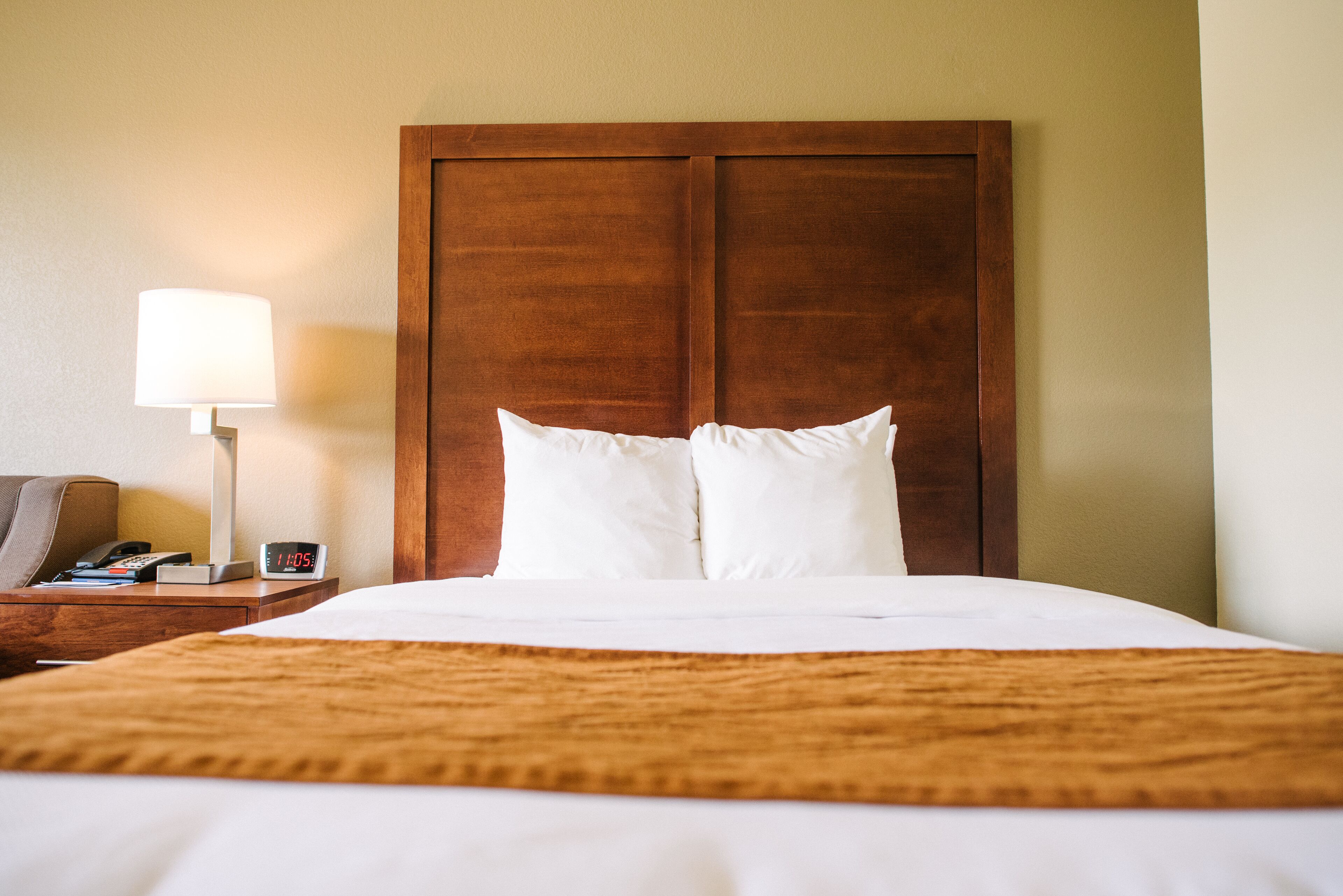 A neatly made bed with a wooden headboard, a bedside lamp, and a clock on the nightstand.
