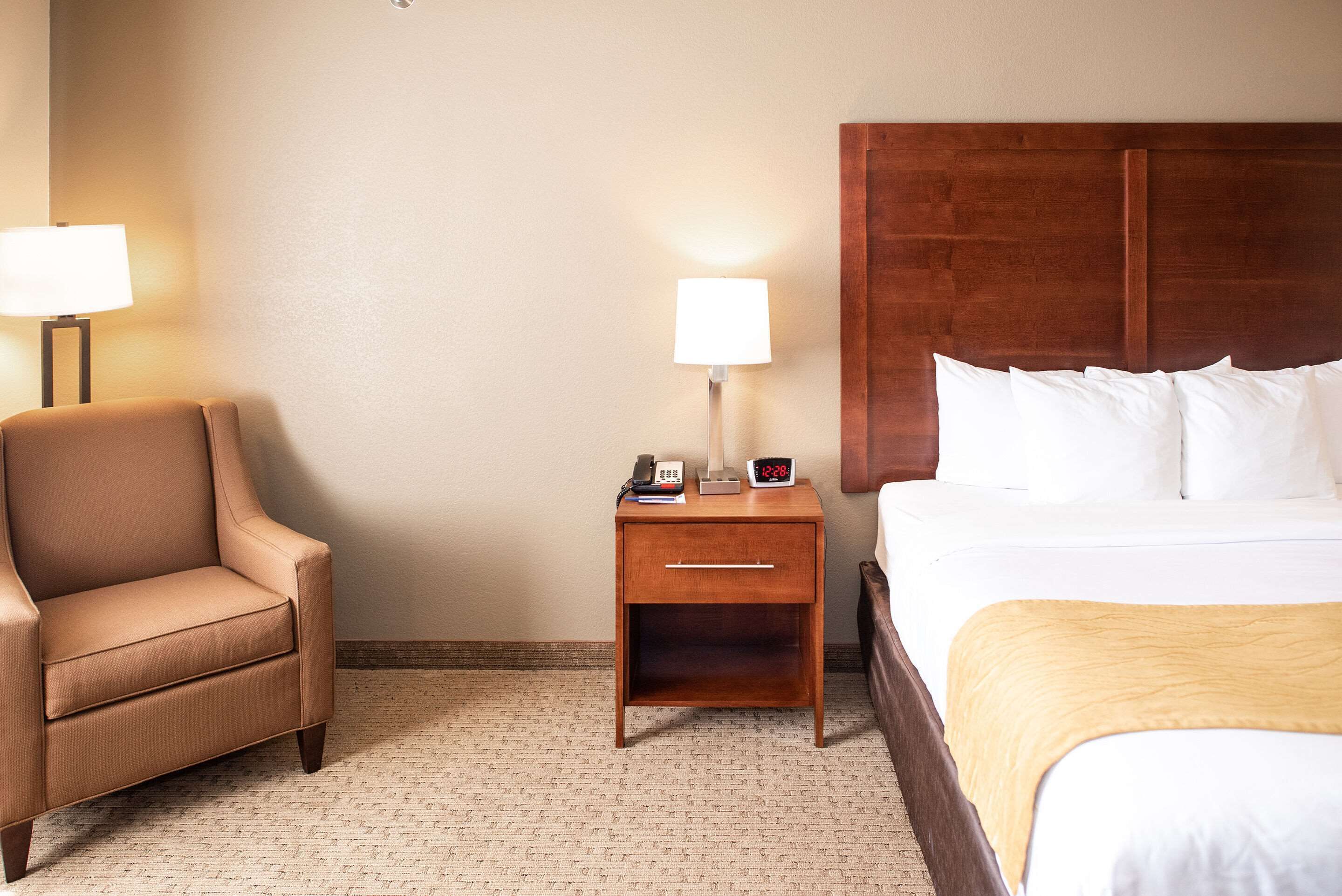 A hotel room with a bed, a nightstand with a lamp, and a chair.