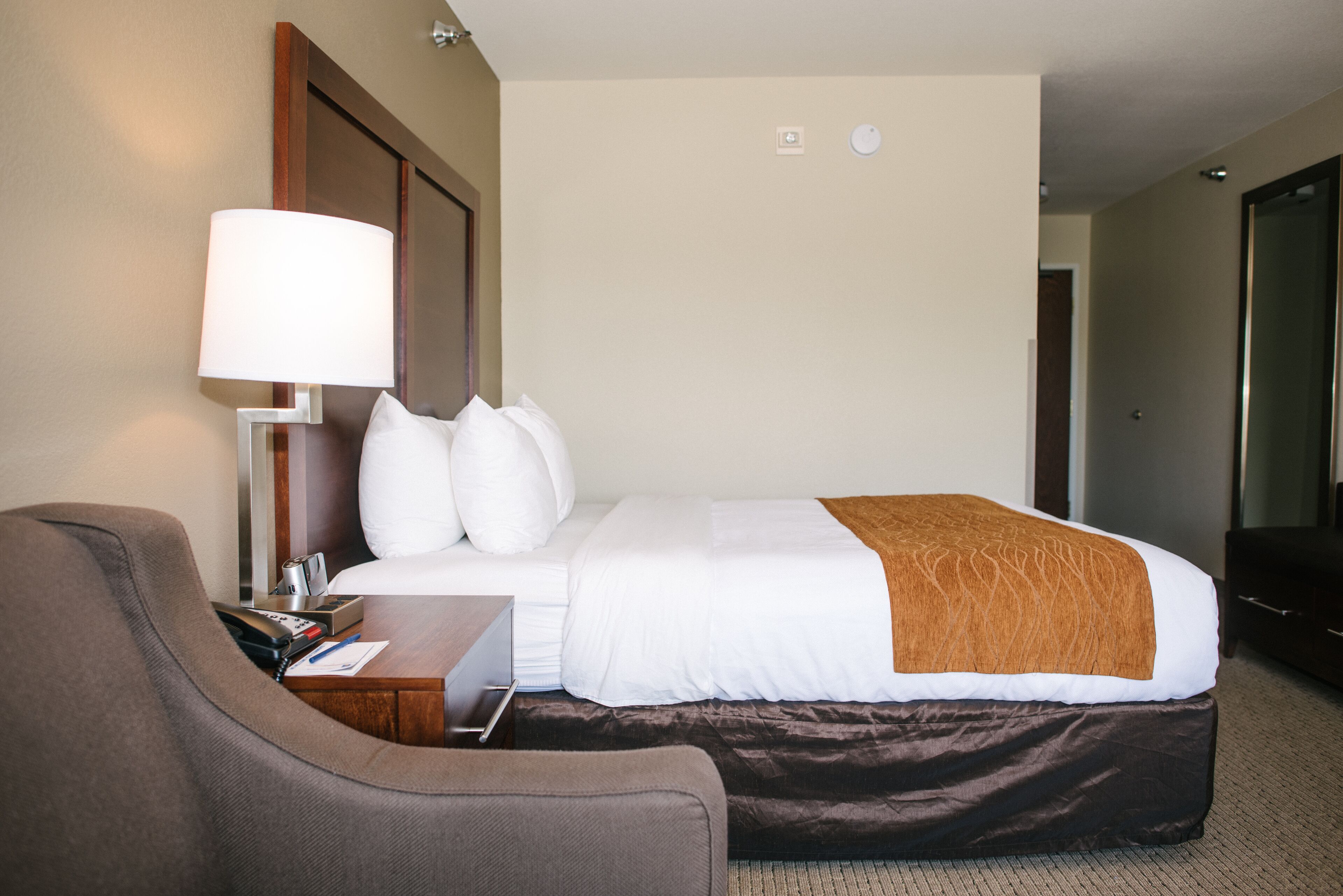 Quarto de hotel com uma cama, uma mesa, uma lâmpada e uma cadeira.