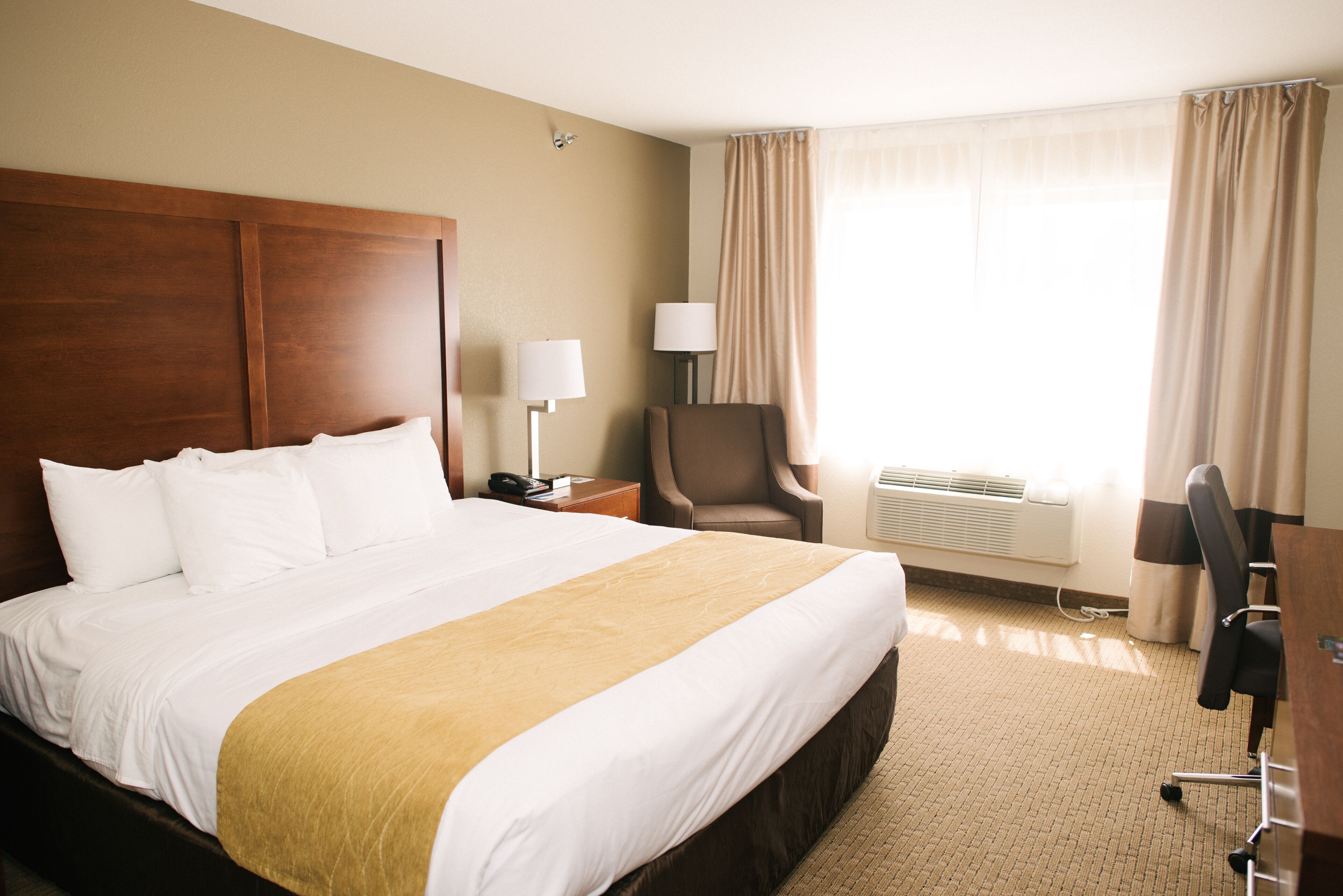 A hotel room with a large bed, a desk, a chair, and a window with curtains.