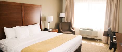 A hotel room with a large bed, a desk, a chair, and a window with curtains.