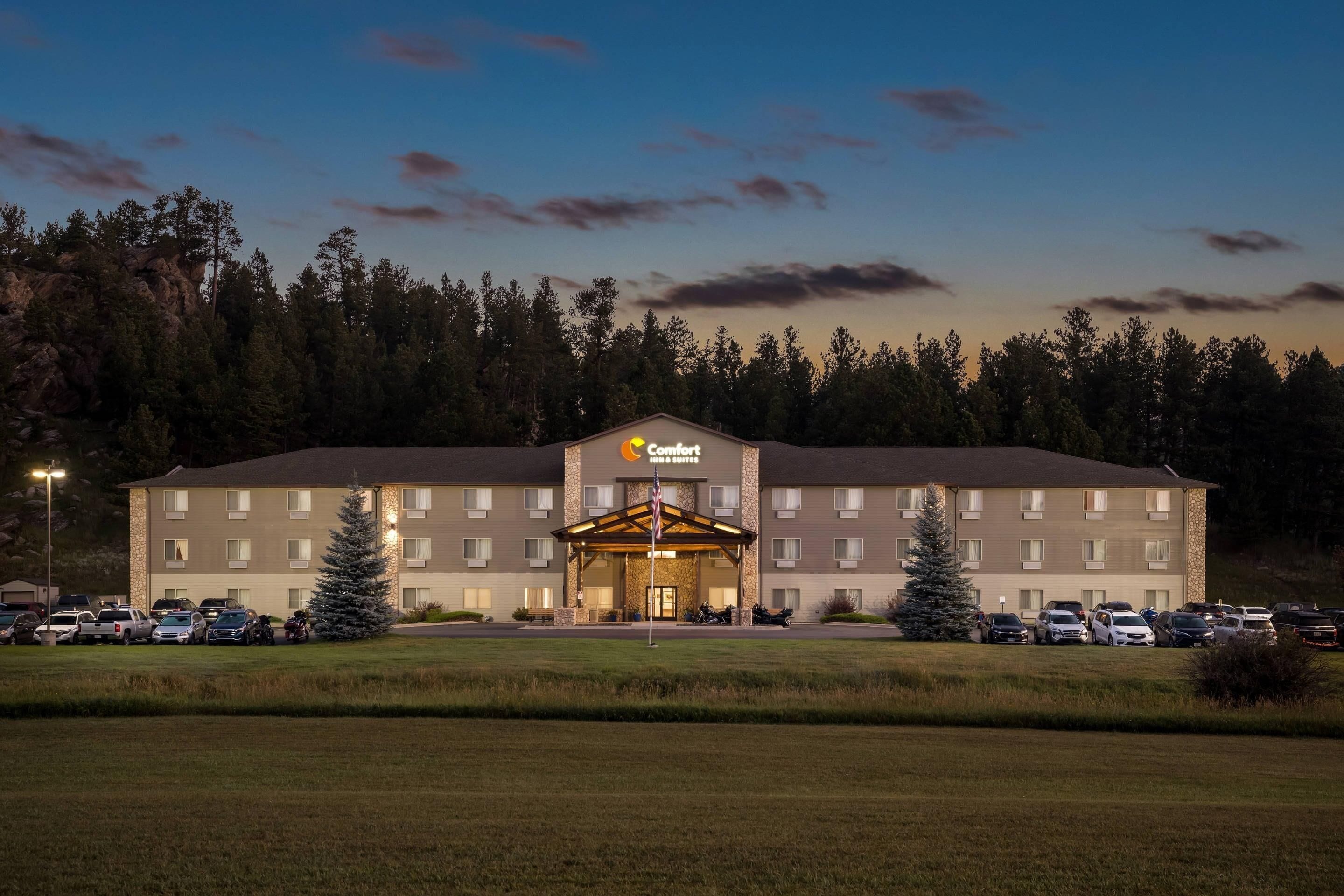 A Comfort Inn hotel with a central entrance, parking lot, and surrounding trees.