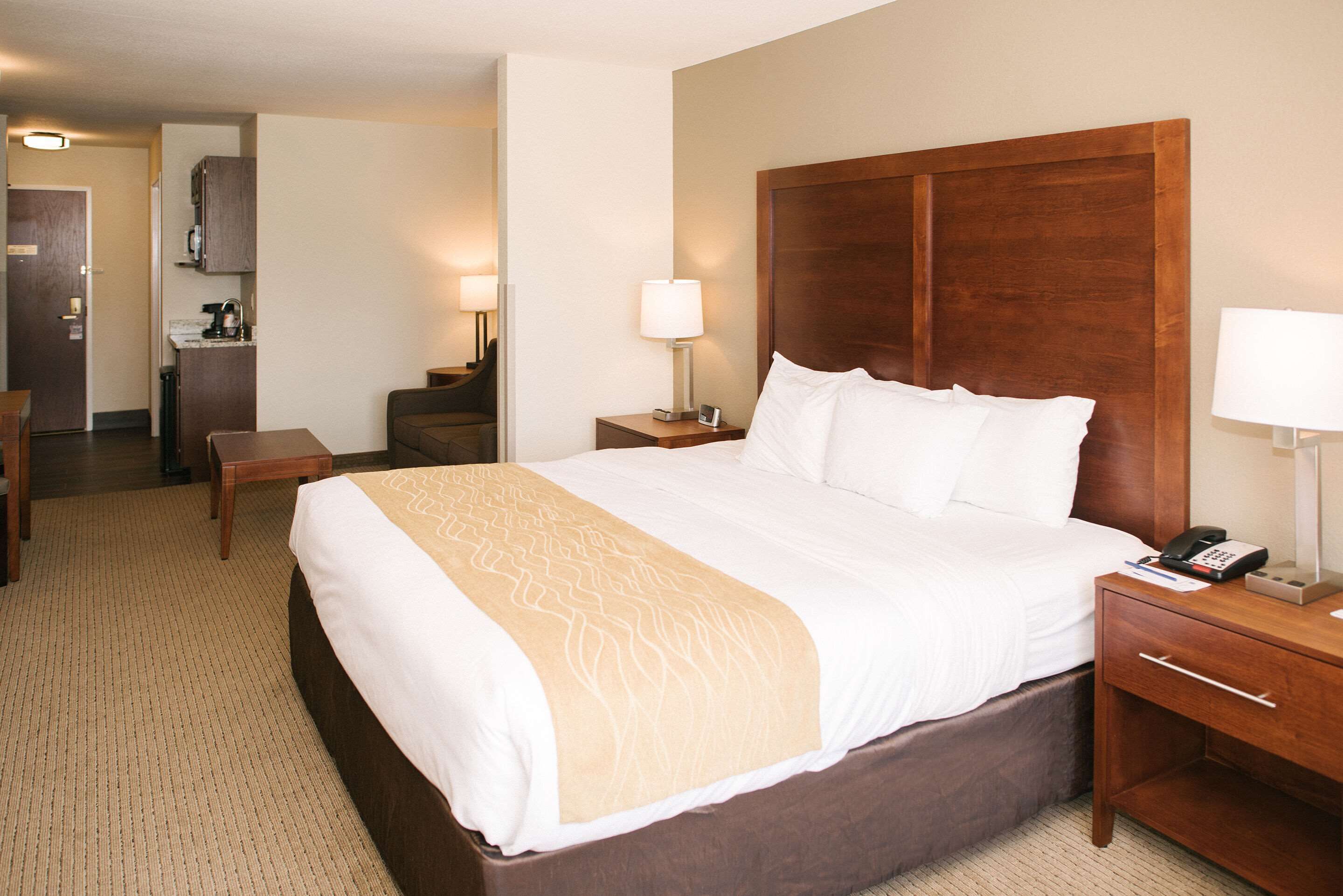 Habitación de hotel con una cama grande, una mesita de noche con lámpara, una mesita auxiliar y un escritorio con silla.