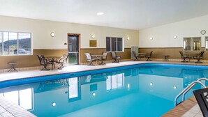 A swimming pool with lounge chairs and tables, a clock on the wall, and a sign indicating pool rules.