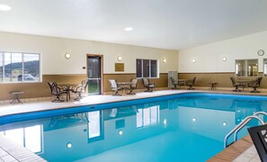 A swimming pool with lounge chairs and tables, a clock on the wall, and a sign indicating pool rules.