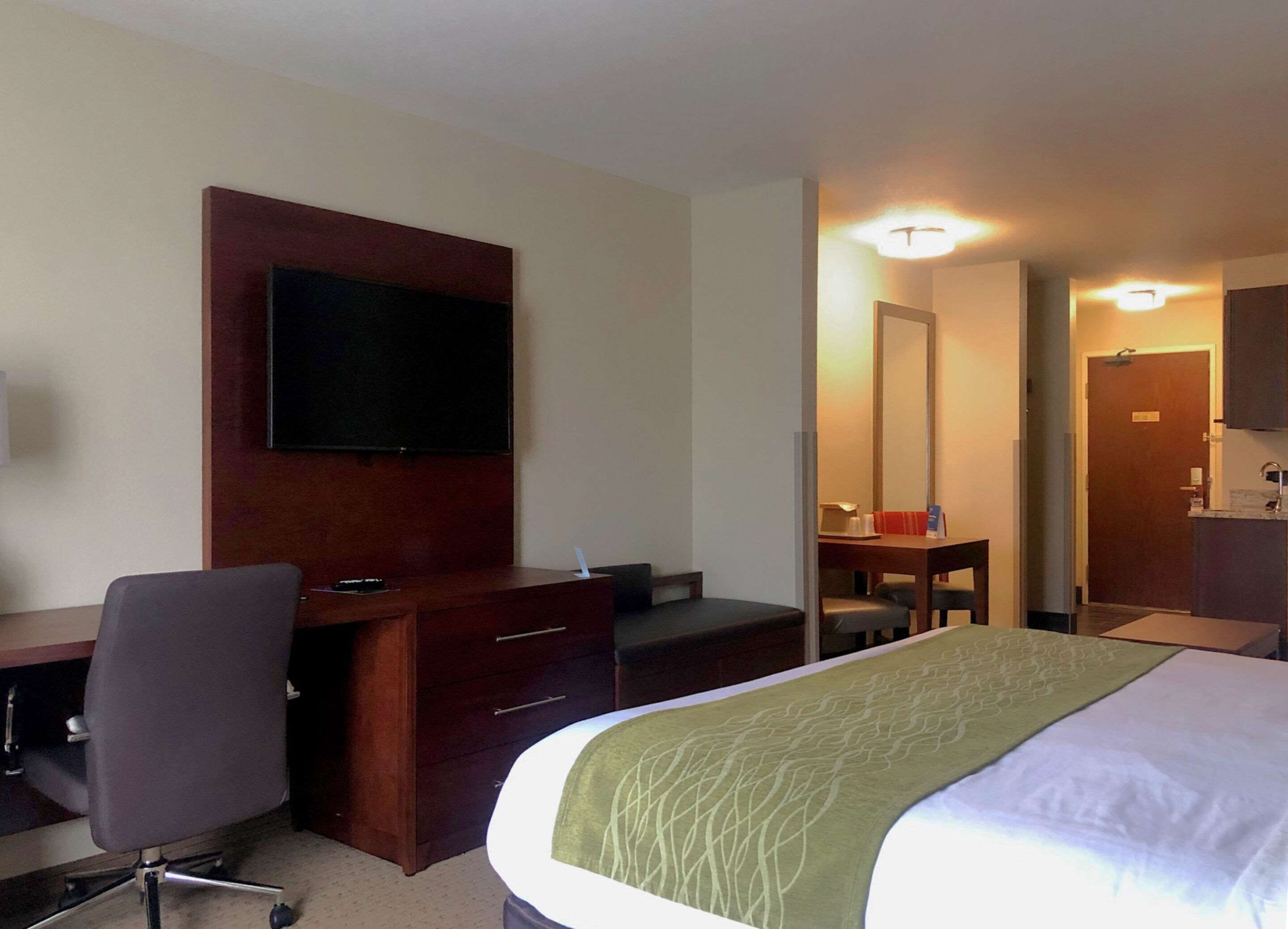 A hotel room with a bed, a desk with a chair, a television, a dresser, and a mirror.