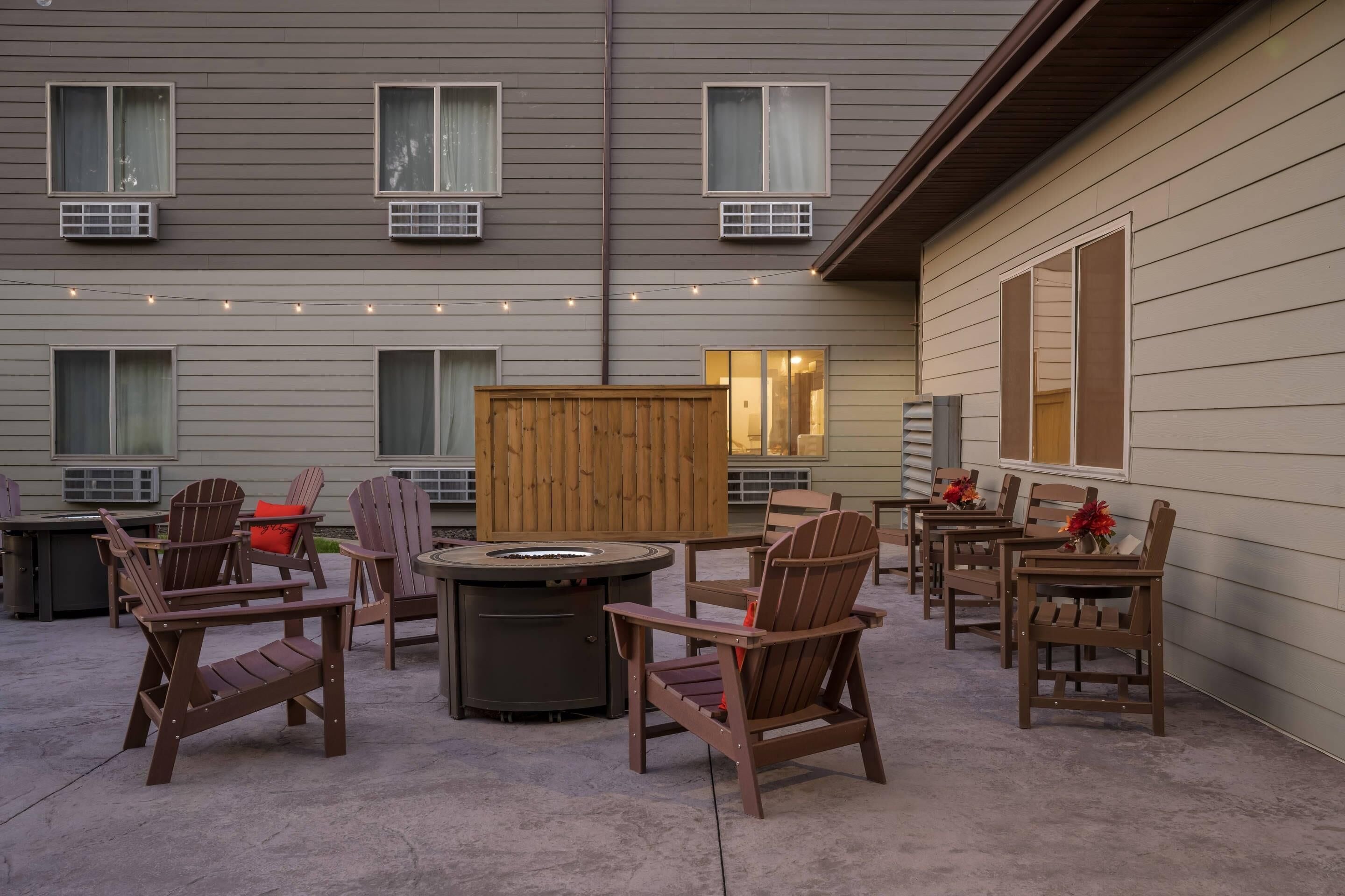 An outdoor patio with Adirondack chairs, a round table, and a wood-burning stove.