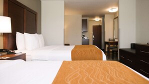 A hotel room with two beds, a desk with a lamp, a dresser, and a mirror.