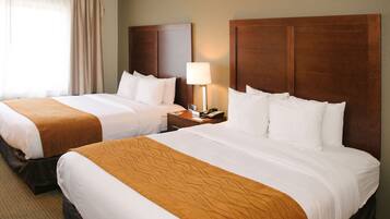 Een hotelkamer met twee bedden, elk met een houten hoofdbord, witte beddengoed en een bruin accent. Er staat een nachtkastje met een lamp en een telefoon.