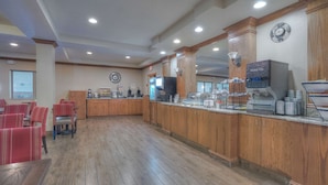 A spacious lobby with wooden flooring, a reception desk, and red chairs.