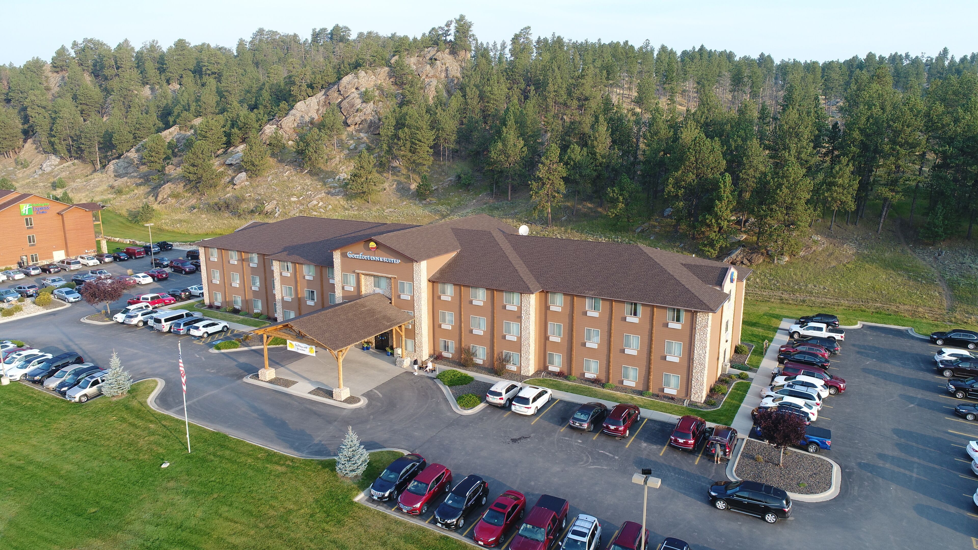 A Comfort Inn & Suites hotel with a parking lot, a covered walkway, and a mountainous backdrop.