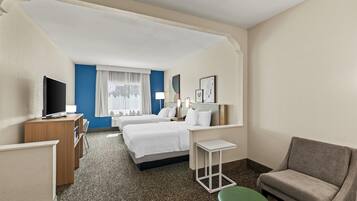 A hotel room with two beds, a desk, a television, a green ottoman, and a chair.