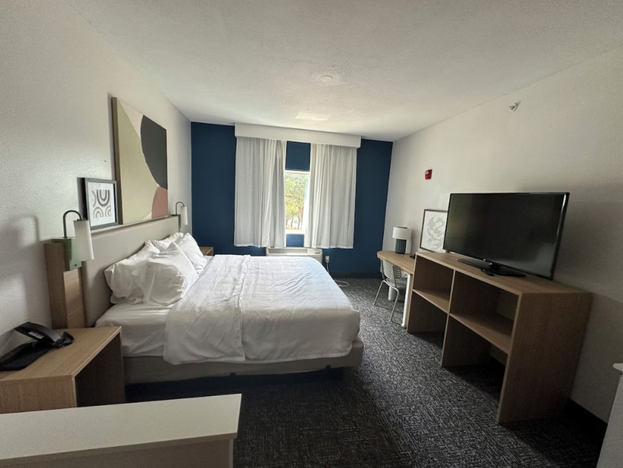A hotel room with a bed, a desk, a TV, and a window with curtains.