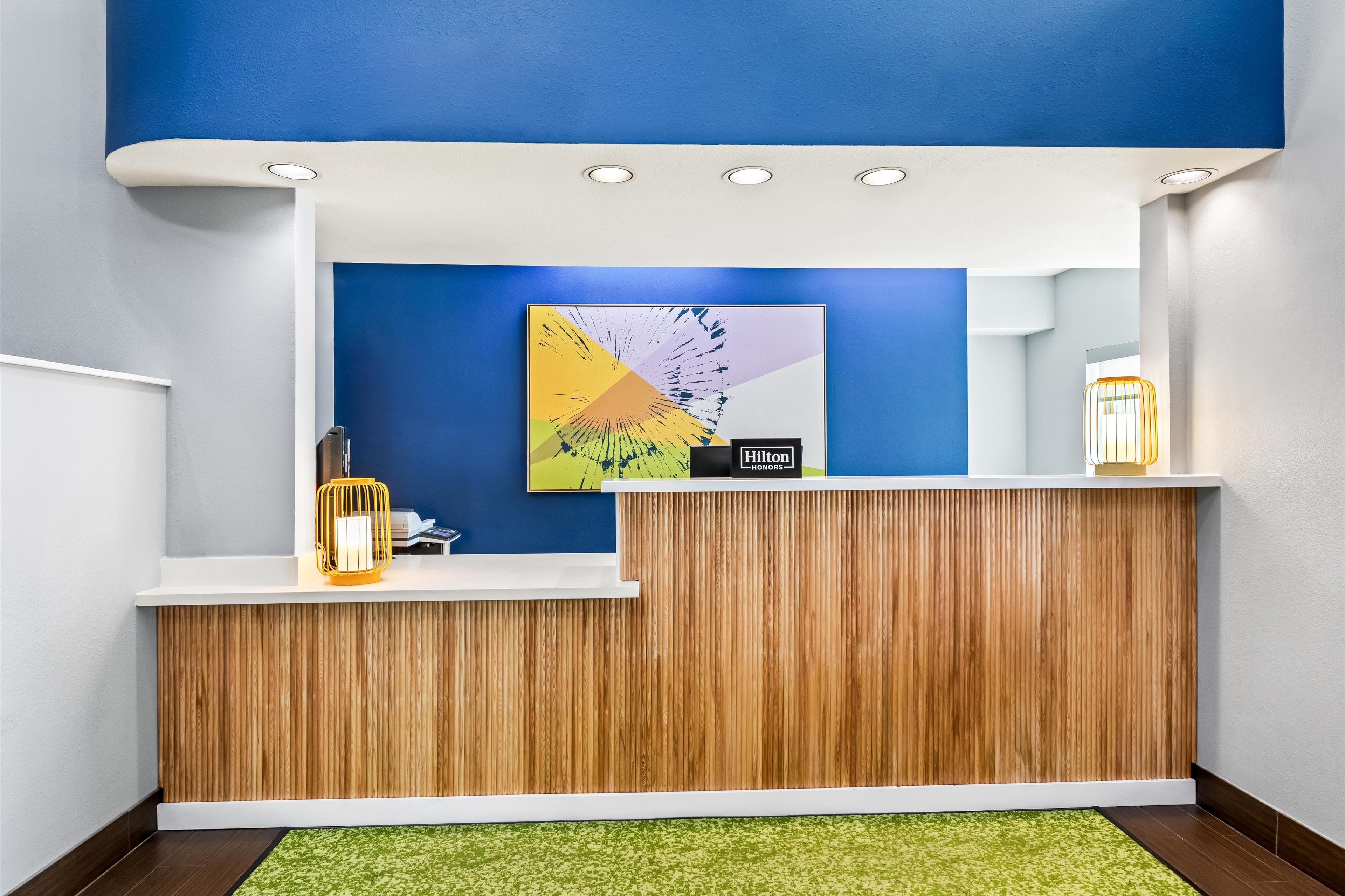 A hotel reception area with a wooden reception desk, a blue wall, and a modern artwork.
