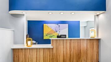A hotel reception area with a wooden reception desk, a blue wall, and a modern artwork.