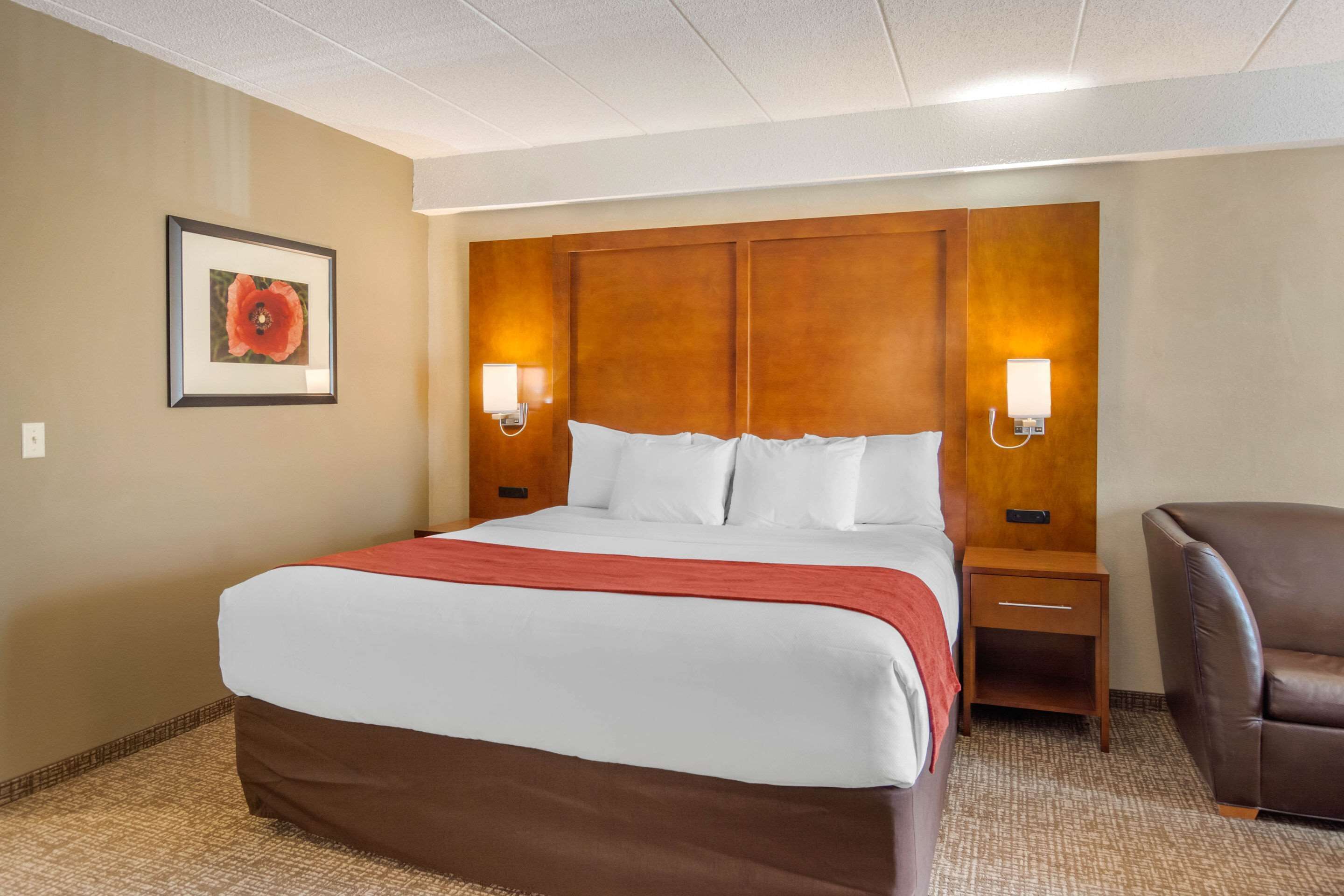 A hotel room with a large bed, two bedside tables, a brown leather chair, and a framed picture on the wall.