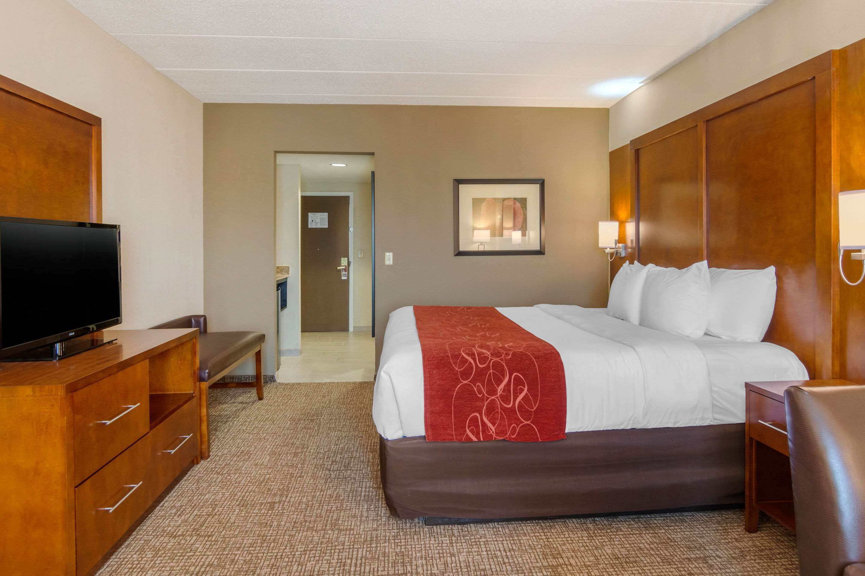 Ein Hotelzimmer mit Bett, Fernseher, Schreibtisch und einer Bank.