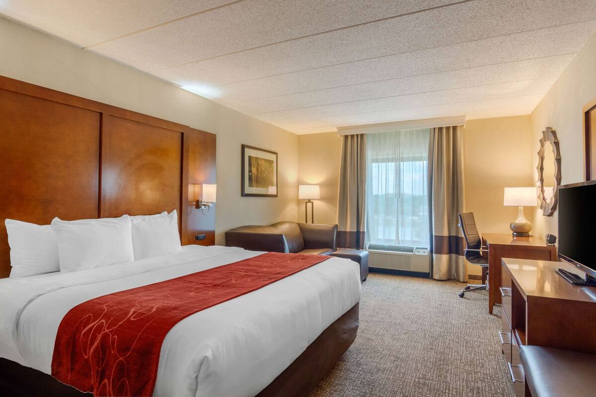 Une chambre d’hôtel avec un grand lit, un bureau, une chaise, une télévision et une fenêtre avec des rideaux.