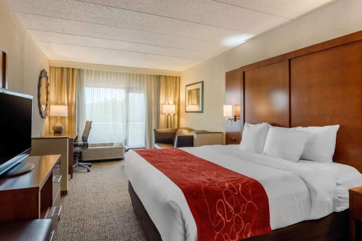 Une chambre d’hôtel avec un grand lit, un bureau avec une télévision, une chaise, une lampe de bureau et une fenêtre avec des rideaux.