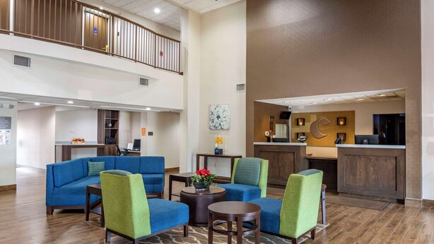A spacious lobby with a blue sofa set, green armchairs, and a small coffee table. A kitchen area is visible in the background. - Comfort Suites South Park (Colonial Heights)