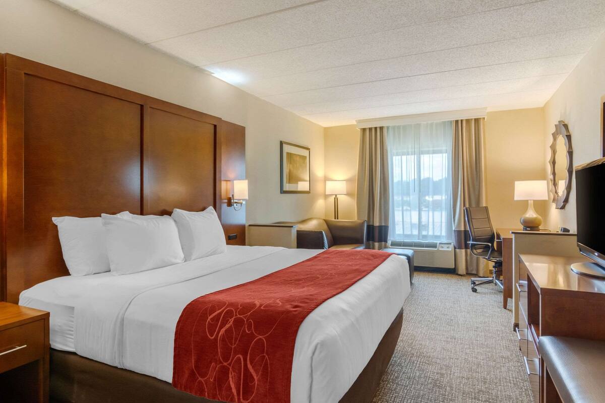 Une chambre d’hôtel avec un grand lit, un bureau avec une chaise, une télévision et une fenêtre avec des rideaux.