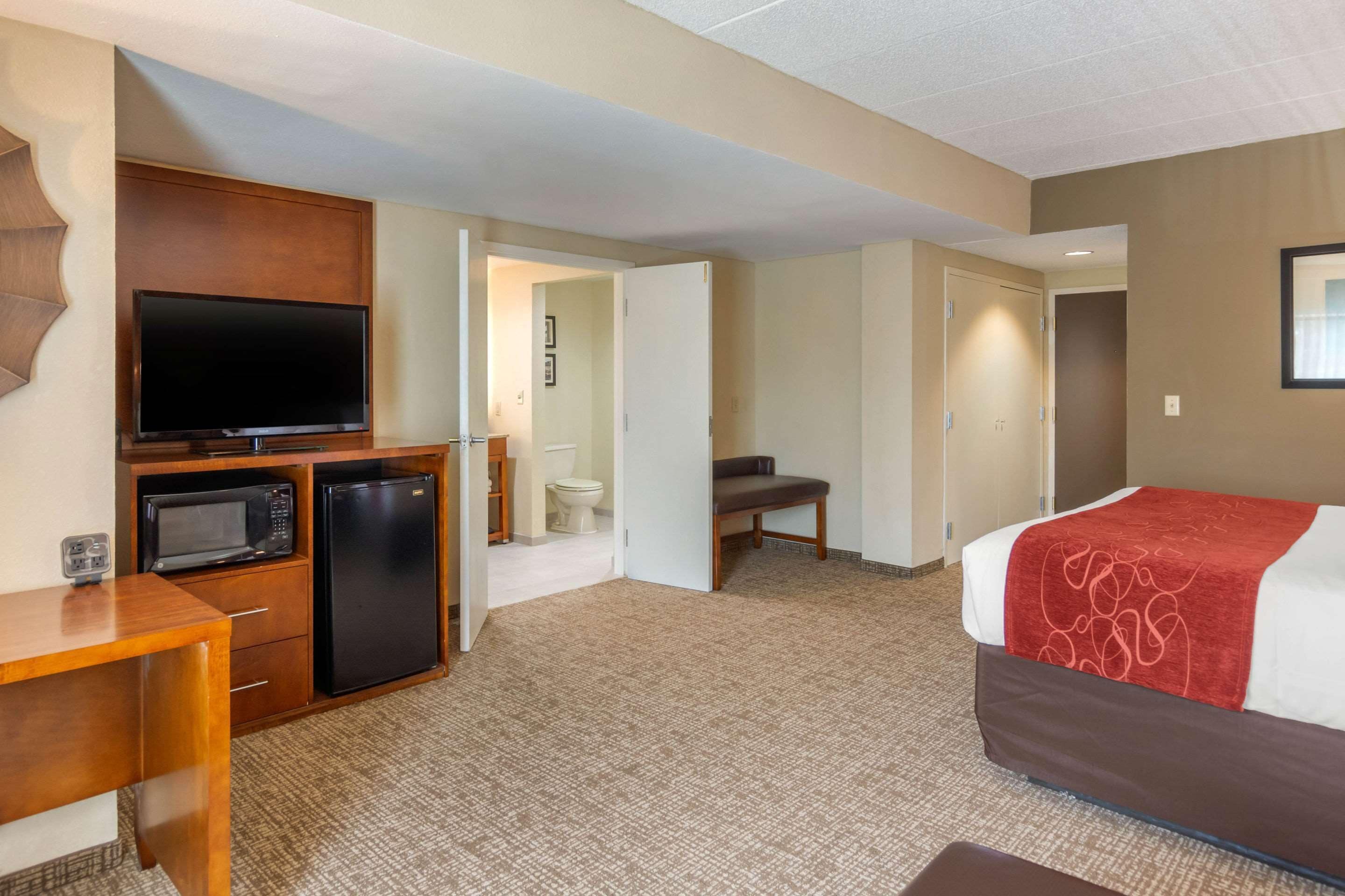 Une chambre d’hôtel équipée d’un lit, d’une télévision, d’un four à micro-ondes, d’un réfrigérateur, d’un bureau et d’une salle de bain, le tout visible à travers une porte ouverte.