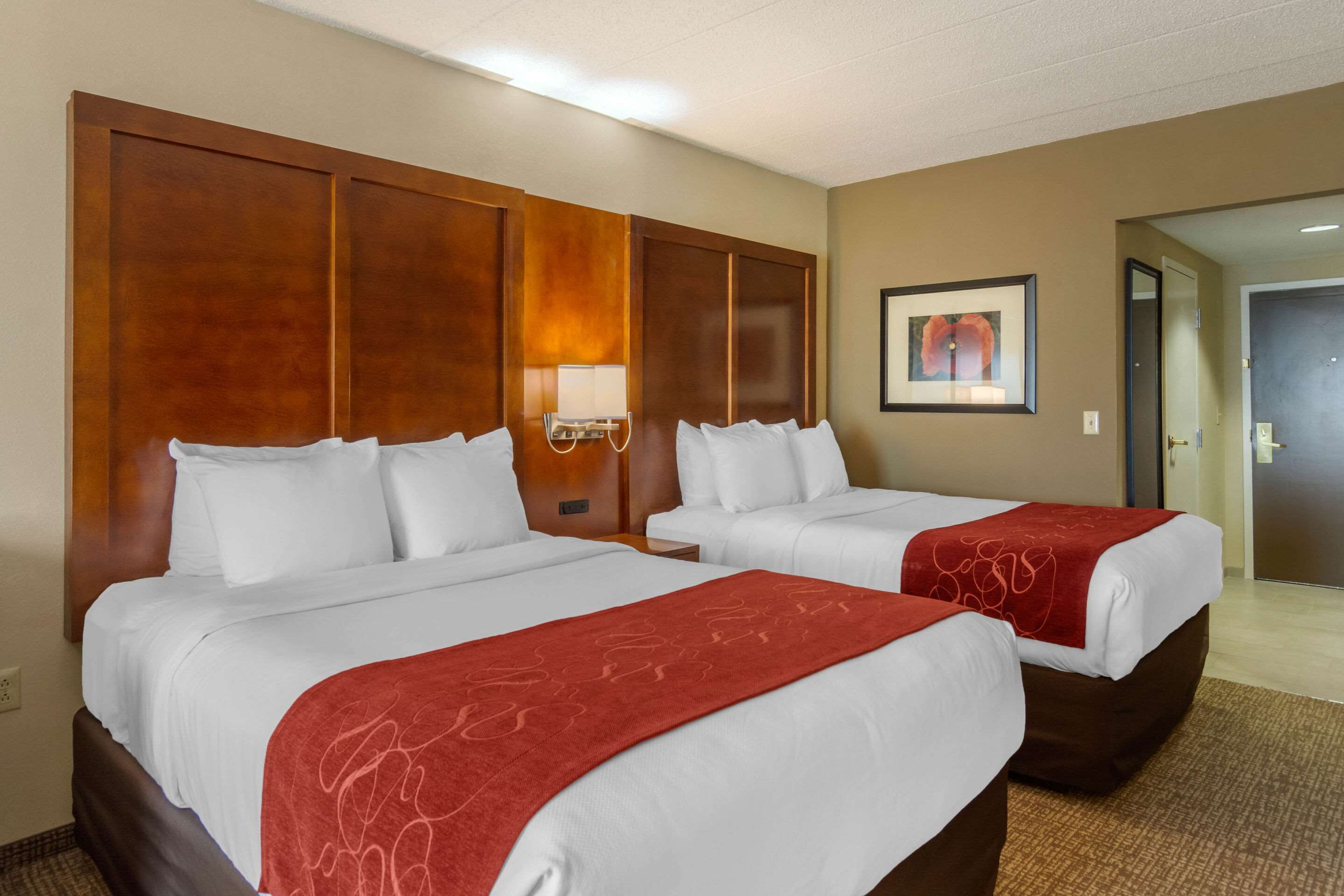 Ein Hotelzimmer mit zwei Betten, einem Holz-Kopfteil, einer Wandlampe und einem gerahmten Bild.