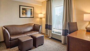 A hotel room with a brown leather sofa, a matching ottoman, a wooden desk, and a framed picture on the wall. - Comfort Suites South Park (Colonial Heights)