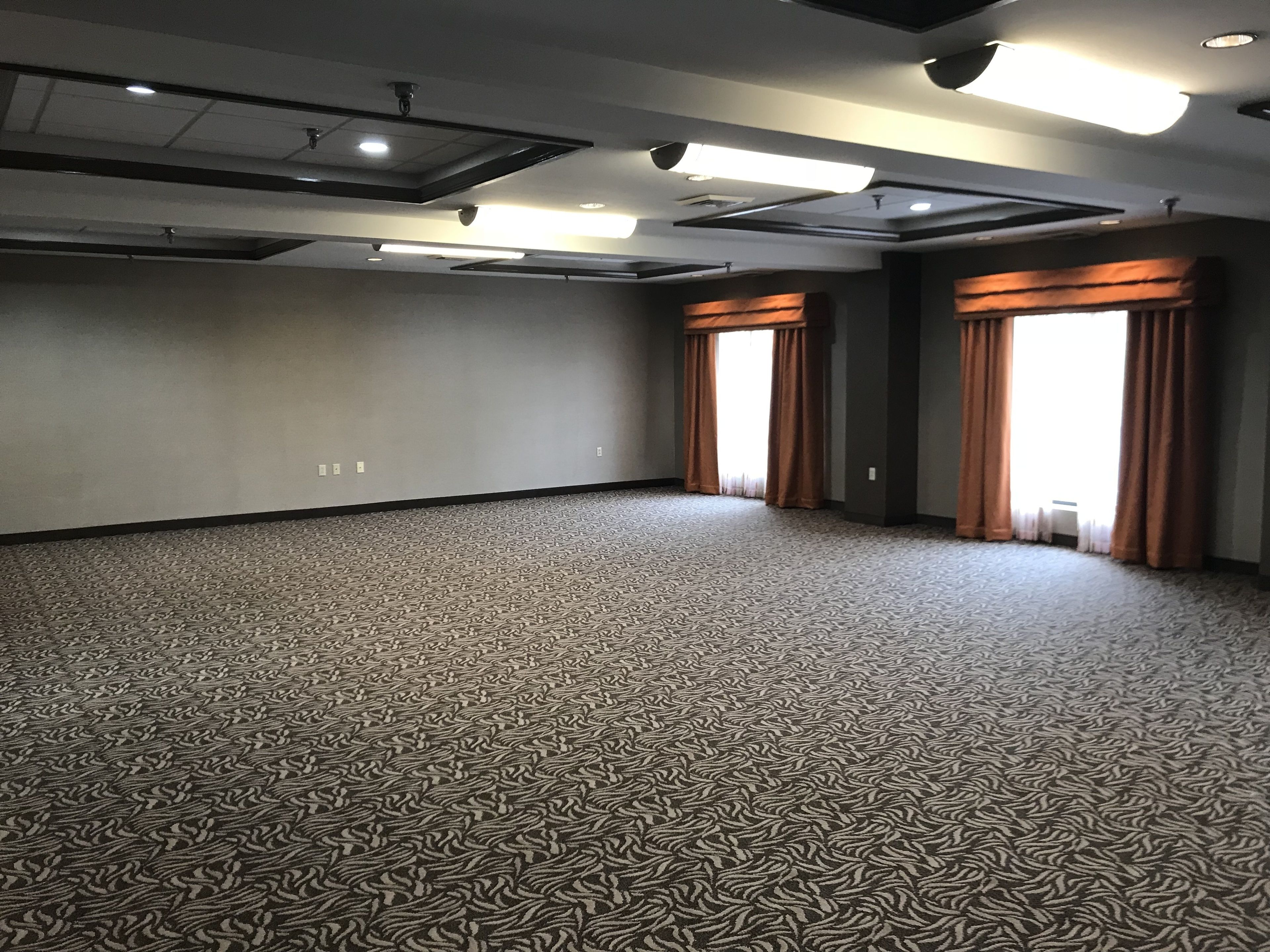 A large, empty conference room with patterned carpet, recessed lighting, and large windows with curtains.