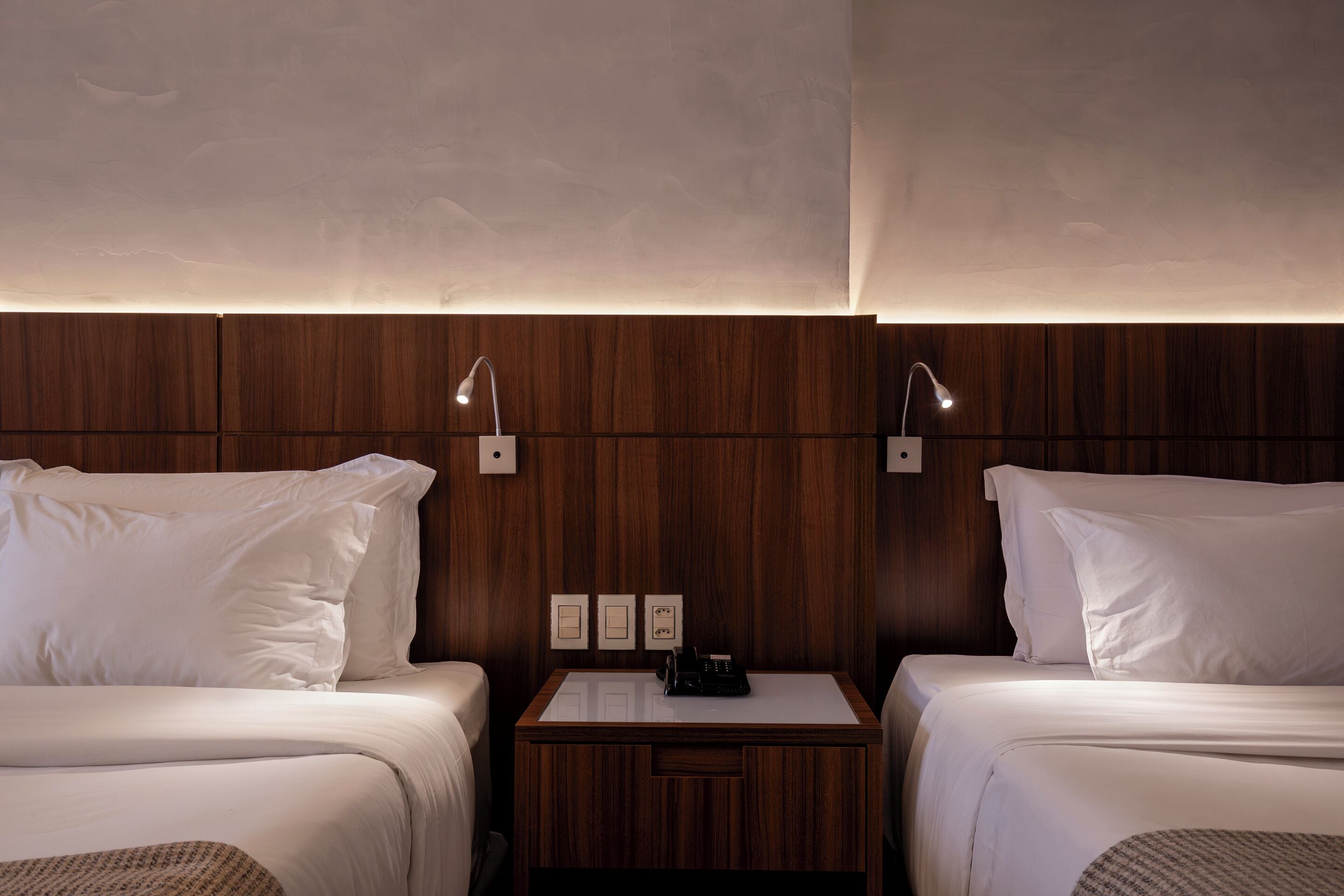 Habitación de hotel con dos camas, cabecero de madera, mesitas de noche y lámparas de pared.