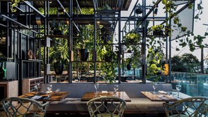 An outdoor dining area with wooden tables and woven chairs, surrounded by a metal structure with hanging plants. - Hotel Gran Marquise (Fortaleza)