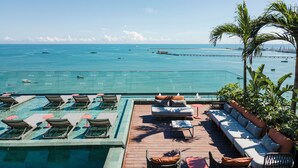 Un área de piscina en la azotea con sillones de descanso y un sofá, con vistas al mar tranquilo, barcos y un muelle.