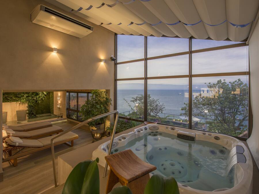 A spa area with a hot tub, lounge chairs, and a view of the sea.